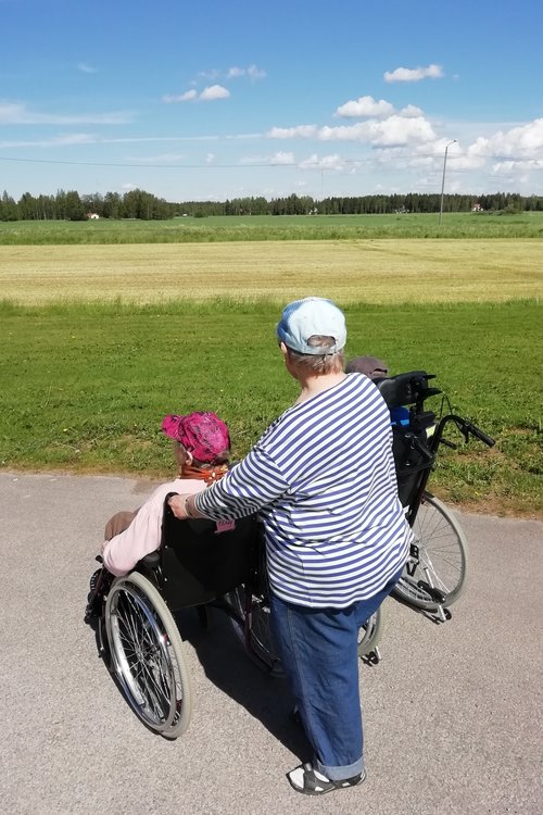 Kesäpäivä peltoaukea pyörätuoli ja saattaja katsovat maisemaa